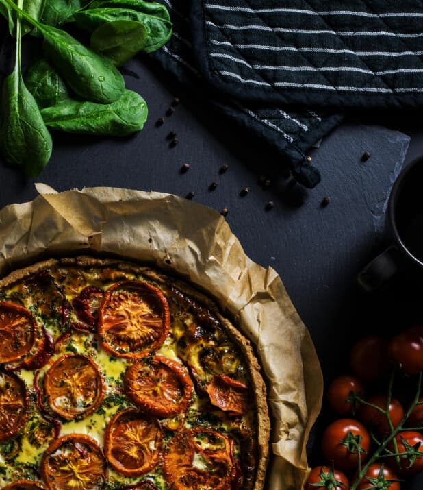 A savory tomato and basil tart on a dark, rustic surface surrounded by fresh ingredients.